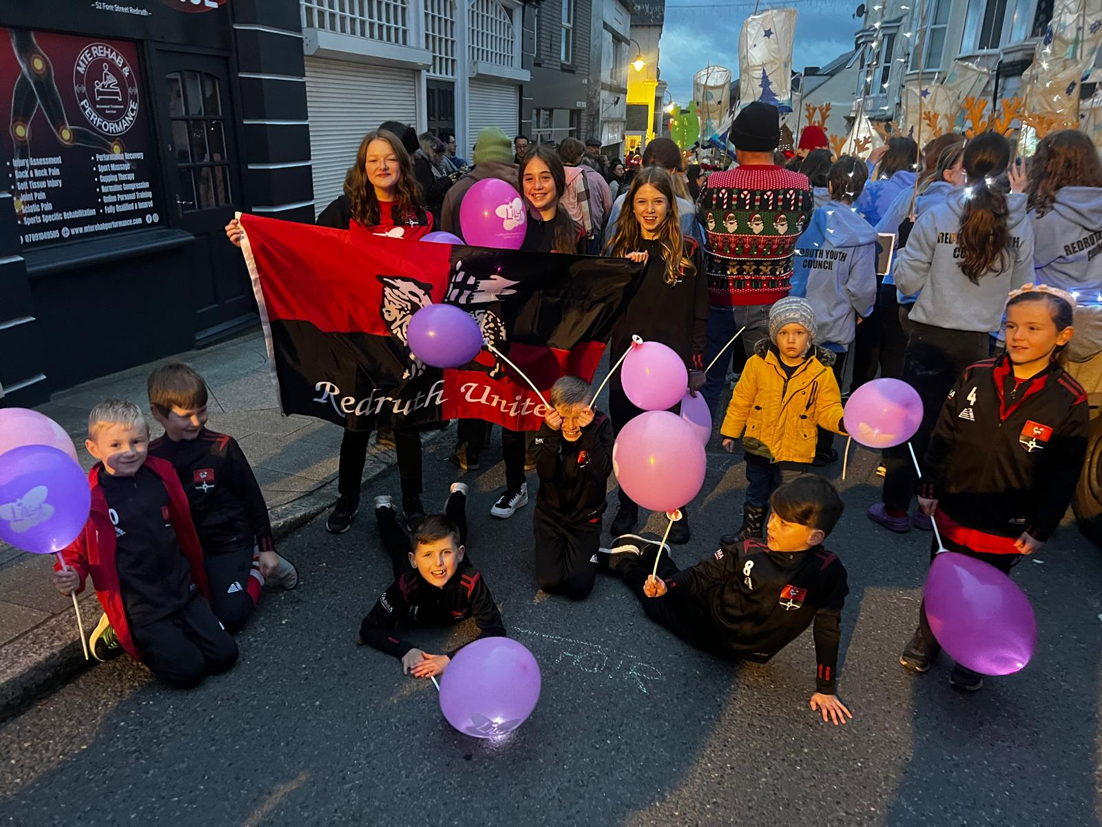 Redruth United youth players with club flag and Lily Foundation balloons at the Redruth town lantern parade