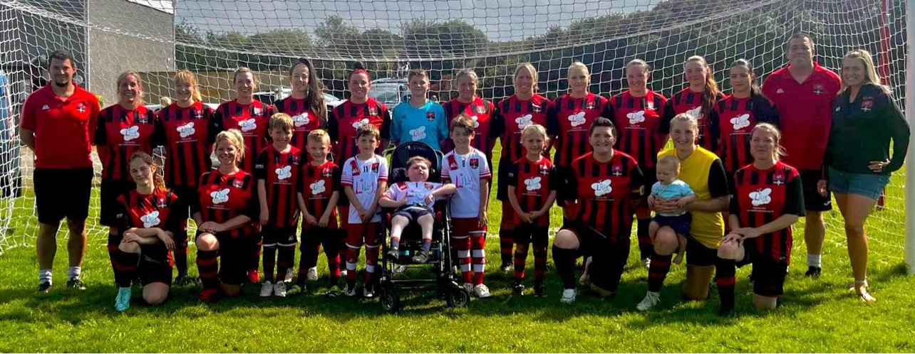 Redruth United women's squad, coaches and young supporters lined up in front of the goal at Clijah Park