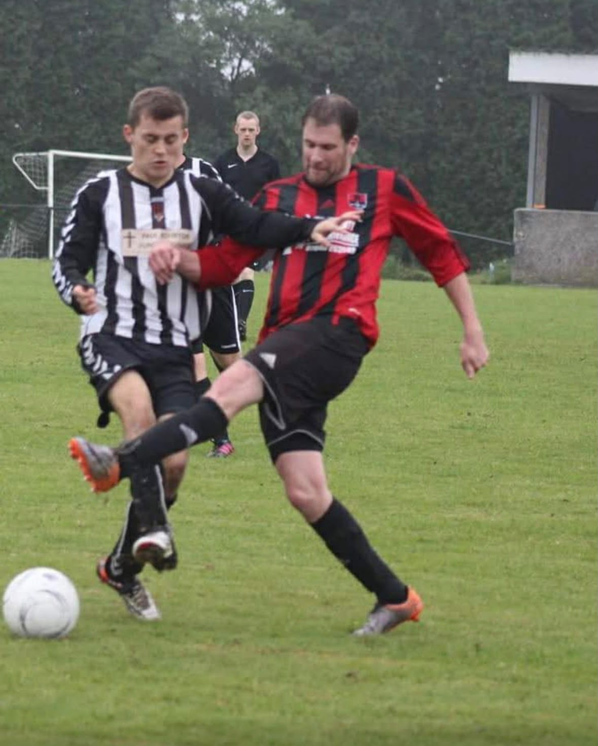 Simon Barrand, Commercial Director, striking the ball in Redruth United's red and black kit